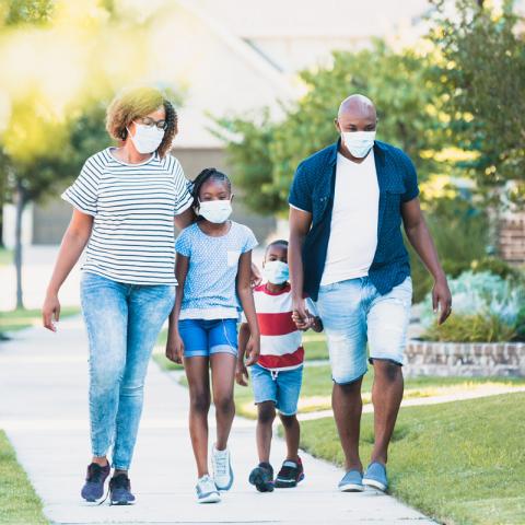 Family walking down the street wearing masks.