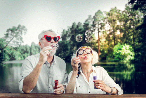 A photo of 2 older adults enjoying themselves blowing bubbles.