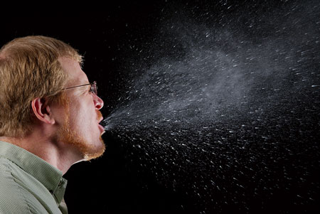 A photo of a man sneezing showing the airborne virus particles.