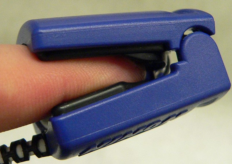 A photo of a pulse oximeter on a light-skinned finger.