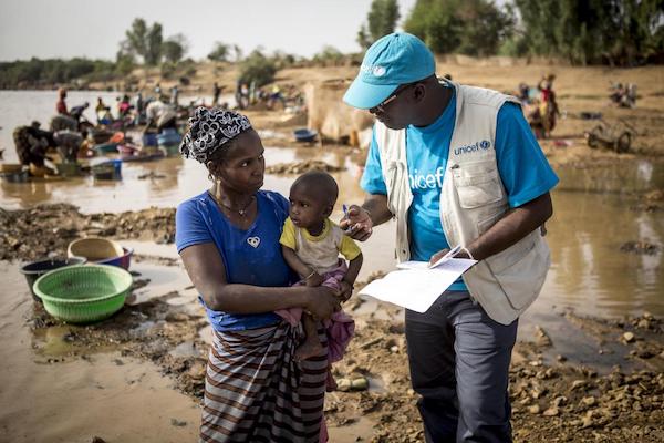 African migrant worker at a gold mine with child talking with UNICEF worker.